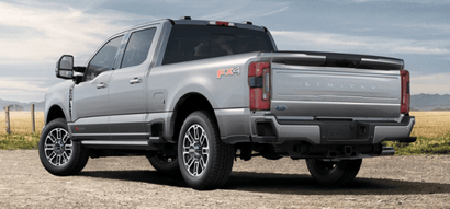 A silver 2024 Ford F-250 Limited shown from the rear and parked on a gravel road, with a fence and field in the background.