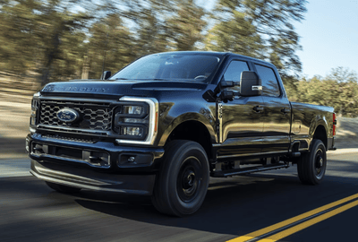 A black 2024 Ford F-250 Super Duty driving down a tree-lined road during the day.