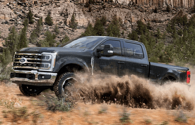 A black 2024 Ford F-250 equipped with the Tremor Off-Road Package and kicking up dirt on a trail.