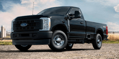 A black 2024 Ford F-250 XL parked on a gravel road, with a field and a silo in the background.