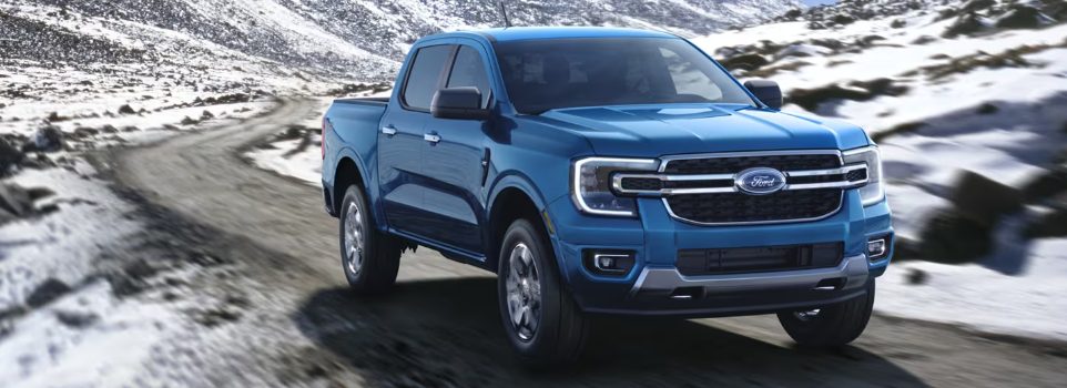 A blue 2024 Ford Ranger driving down a mountain road, with snow visible on the rocks in the distance.