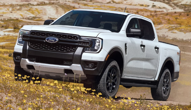 A white 2024 Ford Ranger parked on a grassy hill, with rocks and shrubs in the background.