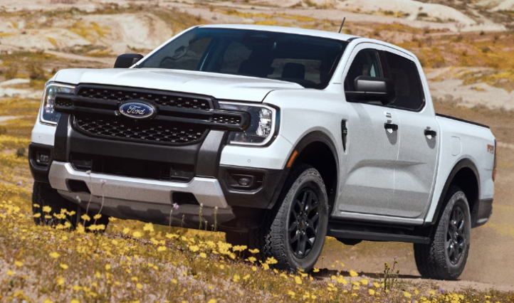 A white 2024 Ford Ranger parked in a grassy hill, with rocks and shrubs in the background.