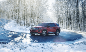 A red 2024 Ford Explorer driving down a snowy road, with trees visible in the background.