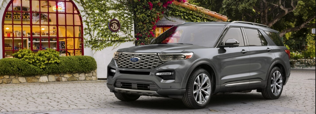 A grey 2024 Ford Explorer Platinum parked on a cobblestone driveway outside of a shop.The building has ivy growing on it and a large red-framed window.