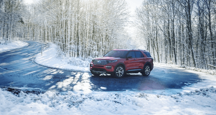 A red 2024 Ford Explorer driving down a tree-lined road, with snow visible on both sides.