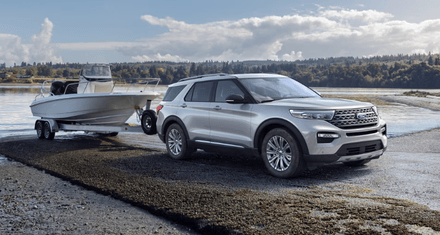 A white 2024 Ford Explorer Platinum parked on the edge of a lake, with a boat hitched to it.