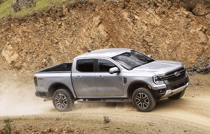 A silver 2024 Ford Ranger driving down a dirt road, with a trail of dust kicked up behind it.