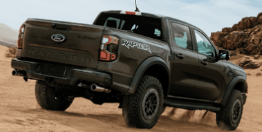 A green 2024 Ford Ranger Raptor driving down a sand dune, with rocks visible in the background.