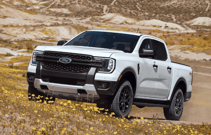 A white 2024 Ford Ranger parked on a grassy hill, with sand and mountains visible in the background.