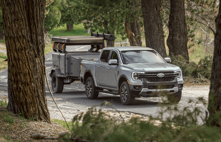 A grey 2024 Ford Ranger towing a trailer down a wooded road.