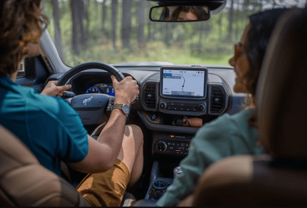 Interior view of the 2024 Ford Bronco Sport Badlands, with a man and woman sitting in the front and a forest visible through the windshield.