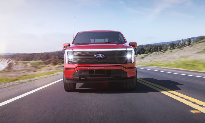 A red 2024 Ford F-150 Lightning driving down a coastal road.