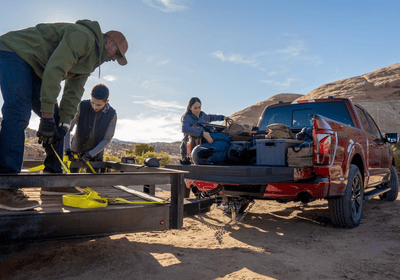 Three people putting various items into the back of a red 2024 Ford F-150, as well as a trailer.