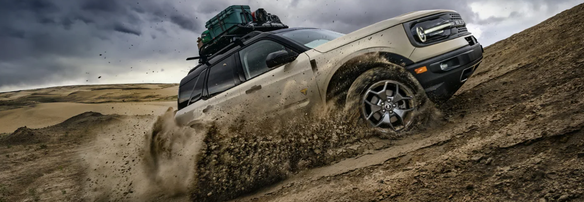 A tan 2024 Ford Bronco Sport Badlands kicking up dirt as it drives up a sand dune.