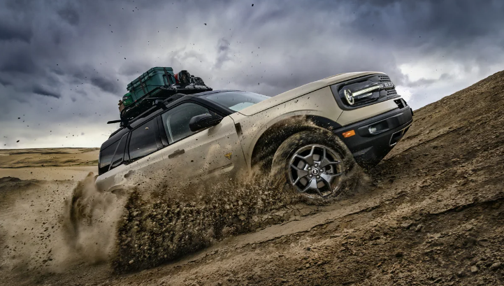 A tan 2024 Ford Bronco Sport Badlands kicking up dirt as it drives up a sand dune.