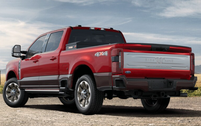 A red 2024 Ford F-350 King Ranch shown from the rear and parked on a gravel road. A field is visible in the background.