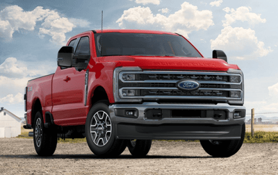 A red 2024 Ford F-350 Lariat parked on a gravel road, with a fence and barn visible in the background.