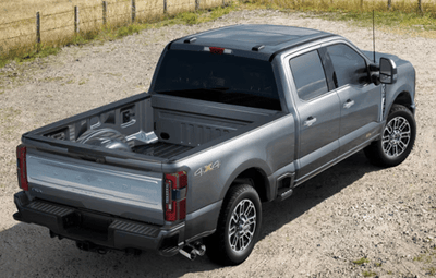 A silver 2024 Ford F-350 Limited parked on a gravel road, with a wire fence and field shown in the background.