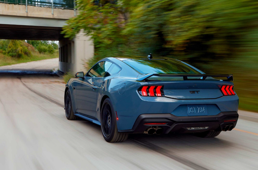 A blue 2024 Ford Mustang GT Premium shown from the rear as it drives down a road.