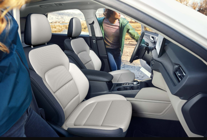 Interior view of the 2024 Ford Escape Platinum, with two people entering the front row. The doors are open to reveal the two-tone seats, dashboard, and steering wheel.