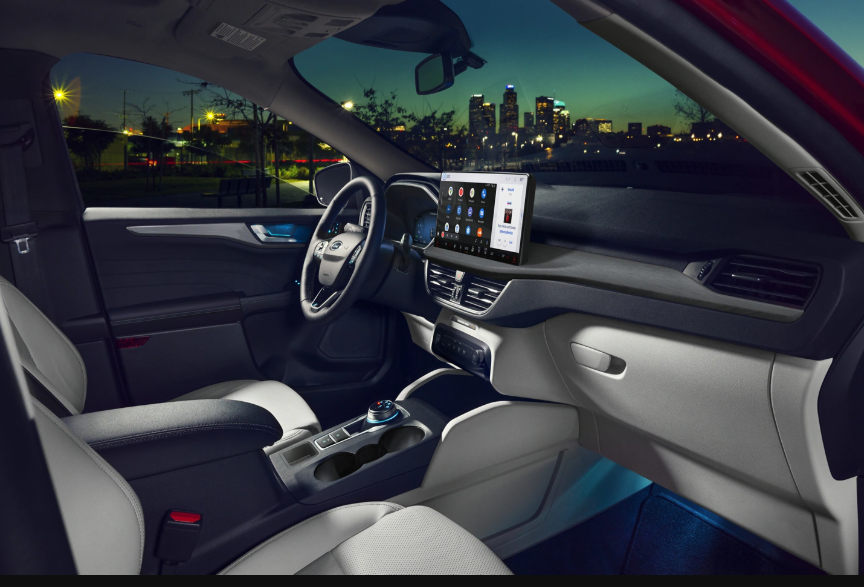 Interior view of the 2024 Ford Escape, showing the seats, steering wheel, and SYNC 4 infortainment console. A city is visible through the windows.