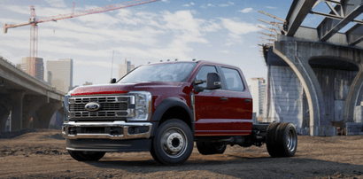 A red 2024 Ford F-550 XL parked on a dirt lot, with a crane visible in the background and a concrete bridge being built to the right.