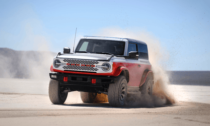 An orange and white 2025 Ford Bronco Stroppe kicking us dust as it drives through a desert.