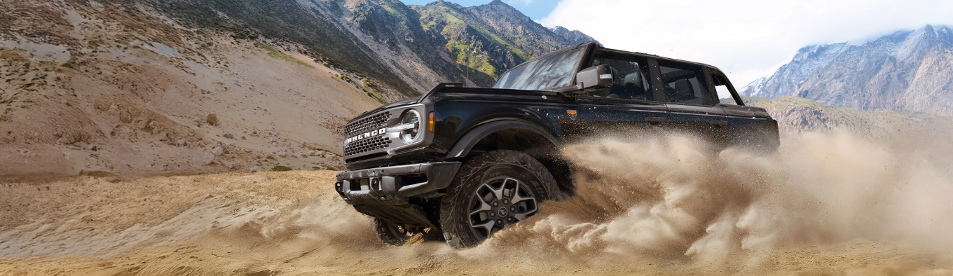 A black 2026 Ford Bronco driving down a sandy hill, with dust kicking up around it.