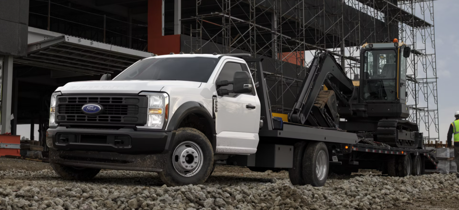 A white 2026 Ford F-550 Super Duty parked at a commercial site, with an excavator sitting in its trailer.