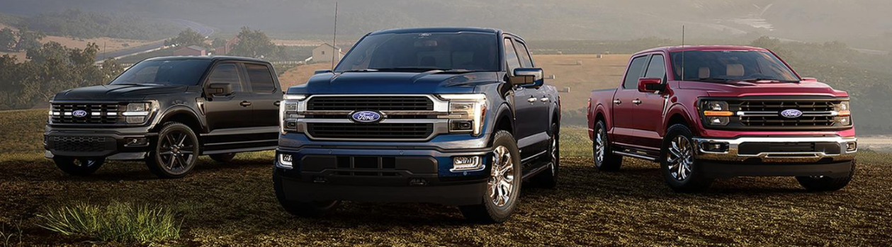 Three 2026 Ford F-150 trucks parked on a dirt road, with a farm visible in the background.