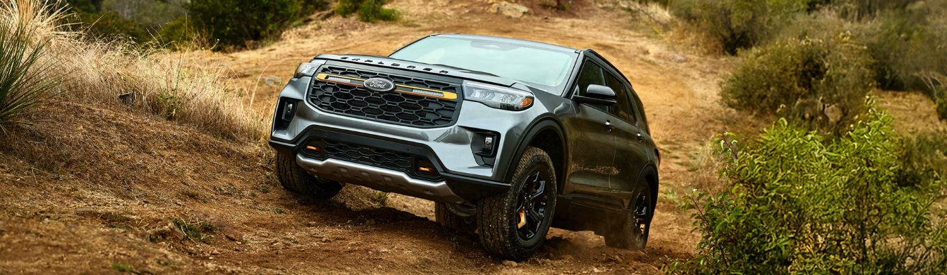 A silver 2026 Ford Explorer Tremor driving up a hill, with rocks and shrubs visible in the background.