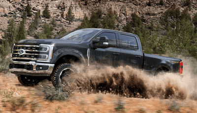 A blue 2025 Ford F-350 King Racnh driving through a desert and kicking up dust.