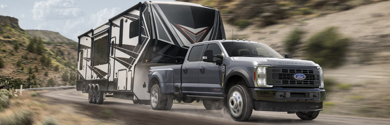 A grey 2025 Ford F-450 Super Duty pulling a camper trailer down a mountain road.