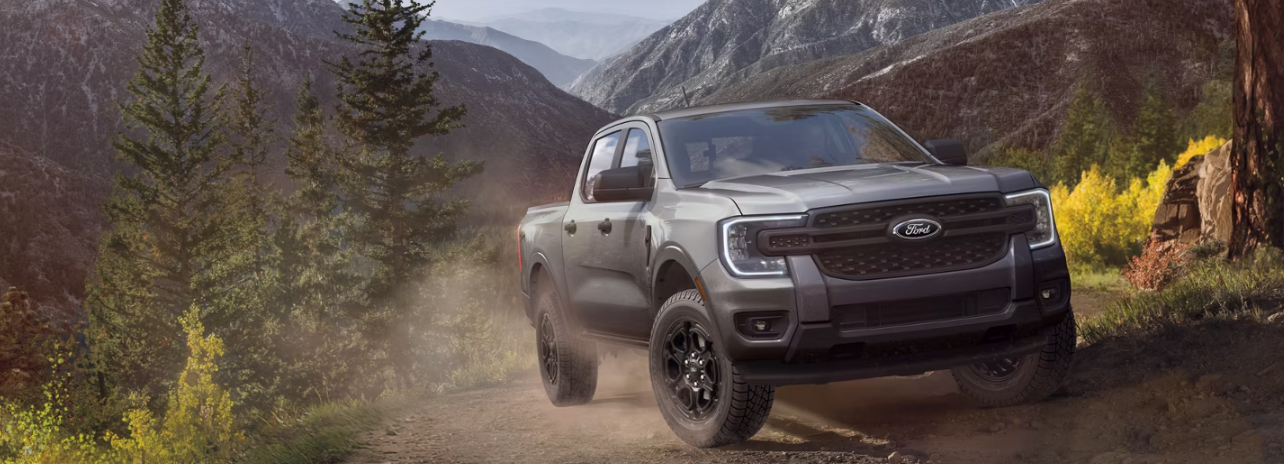 A grey 2026 Ford Ranger driving up a mountain road, with dust trailing behind it.