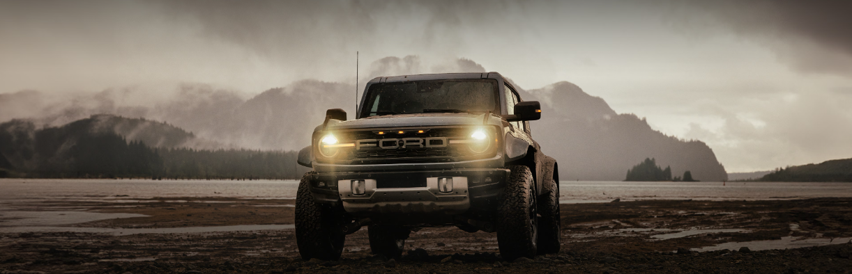 A 2025 Ford Bronco parked in front of a mountain, with heavy fog in the background.
