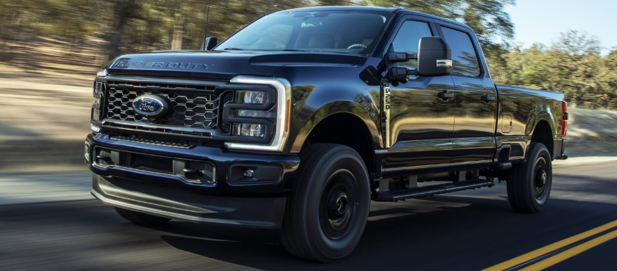 A blue 2025 Ford F-250 driving down a tree-lined road during the day.