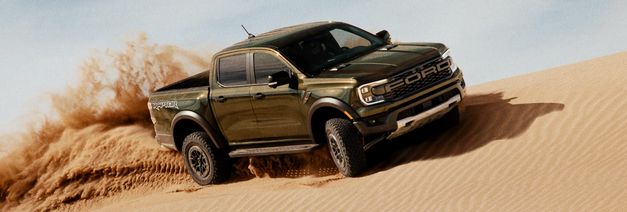 A green 2025 Ford Ranger kicking up a trail of dirt as it drives across a desert. 