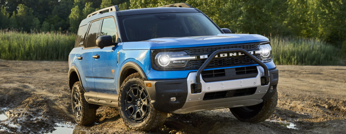 A blue 2025 Ford Bronco Sport parked on a rocky road, with trees and tall grass in the background.