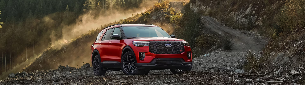 A red 2025 Ford Explorer parked on a gravel road, with mountains visible in the background.