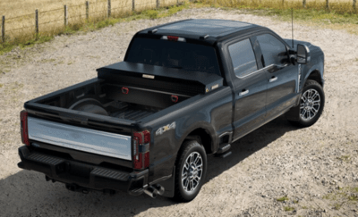 A black 2023 Ford F-350 Limited shown from the rear and parked on a gravel road, with a matte-black toolbox and side-step visible as available options.
