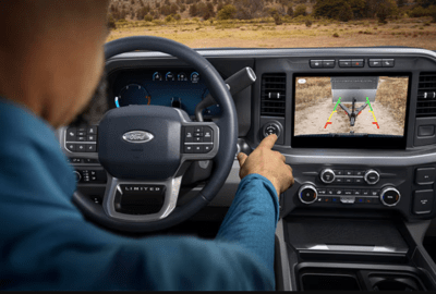 A man using the centre stack on the 2023 Ford F-350 Super Duty, with an image displaying the trailer behind the truck and using colour-coded guidelines to help him navigate.