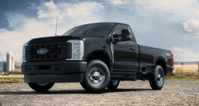 A black 2023 Ford F-350 XL Super Duty truck parked on a gravel road, with clouds, a field, and a silo in the background.