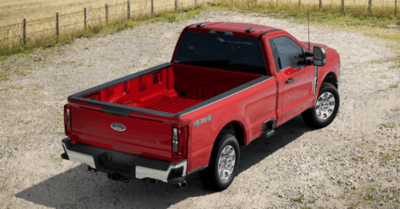 A red 2023 Ford F-350 XLT parked on a gravel road, with a wire fence and field shown in the background.