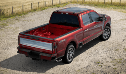 A red 2024 Ford F-350 Limited Super Duty parked on a gravel road and shown from the rear. A fence and field are visible in the background.