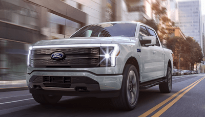 A white 2024 Ford F-150 Lightning driving down a city street during the day.