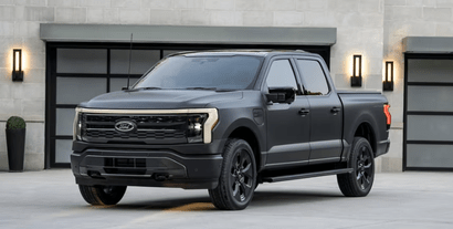 A 2024 Ford F-150 Lightning Platinum equipped with the Black Package and parked in front of a garage door.