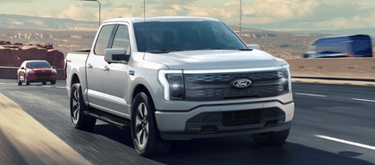 A silver 2024 Ford F-150 Lightning Flash driving down a highway, with various cars surrounding it and mountains visible in the background.