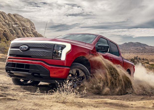 A red 2024 Ford F-150 Lightning kicking up dust in the desert, with mountains visible in the background.