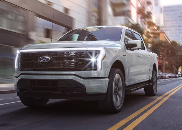 A white 2024 Ford F-150 Lightning driving down a city street.